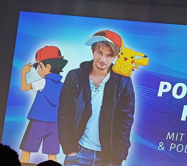 Digitales Bühnen-Design auf der AnimagiC 2024 mit Ash Ketchum, Pikachu und Felix Mayer. Felix trägt eine Ash-Mütze, während das Design die Pokémon-Welt stilisiert darstellt.